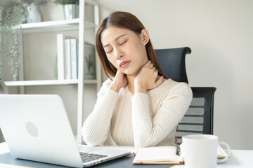 Asian business woman suffering from neck pain working in office sitting at table.