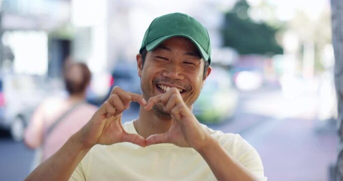 Love, man and face with heart hands for motivation, support or thank you with smile outdoor on city background. Asian person, portrait or loving sign for solidarity, unity and kindness on sidewalk