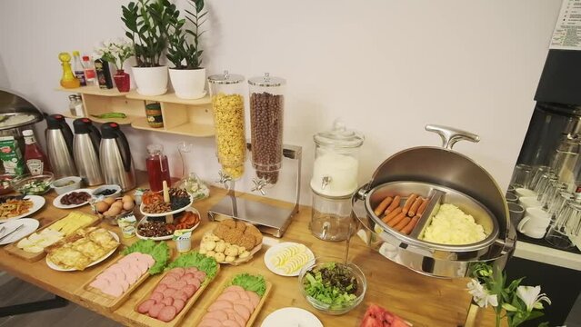 A breakfast table is set in a small hotel. Sausages, yogurt, salads, sauces, drinks
