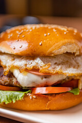 Hamburger with egg and meat, accompanied by french fries, on a plate with creams on a wooden table.