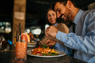 An interracial pair of friends bonding over a delectable lunch at a cozy cafe, their laughter...