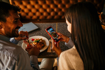A diverse loving couple snapping pictures of their dishes and each other in a cozy cafe setting