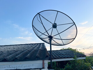 Satellite dish or television antenna on house roof with clear blue sky with clouds.