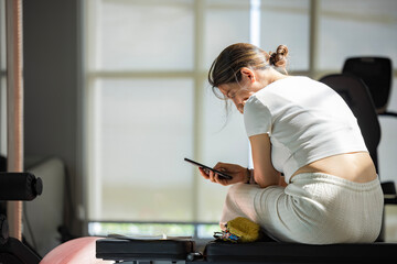 Attractive woman using mobile phone at gym for a workout, training and body wellness with a mobile...