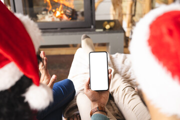 Biracial couple with santa hats having video call on smartphone at christmas at home, copy space