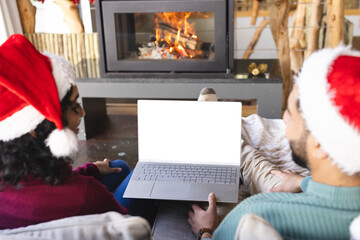 Biracial couple with santa hats having video call on laptop at christmas at home, copy space