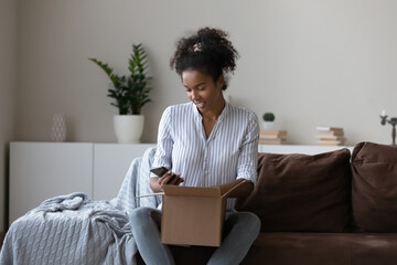 Happy African customer preparing parcel for sending, packing carton box, using smartphone, ordering...