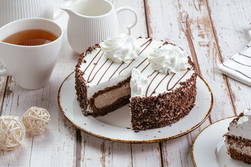 chocolate cake with cream on a plate, tea in a cup, light background