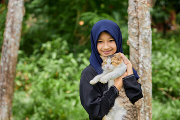 Muslim girl holding cat in garden