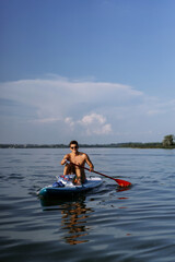 Man in swimming trunks rides paddleboard on a lake in summer. supboard