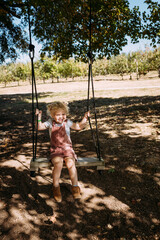 Young child swinging under trees at farm