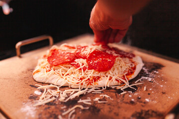 Man finalizing his home made pepperoni pizza - obrazy, fototapety, plakaty