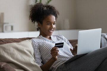 Happy shopaholic girl with laptop using credit card for shopping, online payment, spending money on internet, making transactions on bank app. Customer getting good cashback for purchase - obrazy, fototapety, plakaty