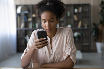 Focused African American Millennial gen Z girl using smartphone, browsing internet on mobile phone,...