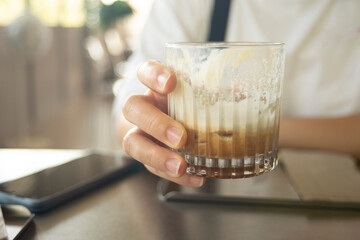 Close up of woman hand holding glass of coffee with ice cubes.