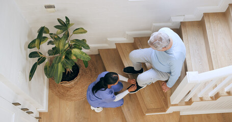 Nurse tie shoes of senior man on stairs at home, help and top view of support. Caregiver tying...
