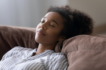 Relaxed young African American woman, peaceful teen girl resting on soft couch at home, sleeping with serene face, breathing fresh cool conditioned air, enjoying relaxation, break. Close up