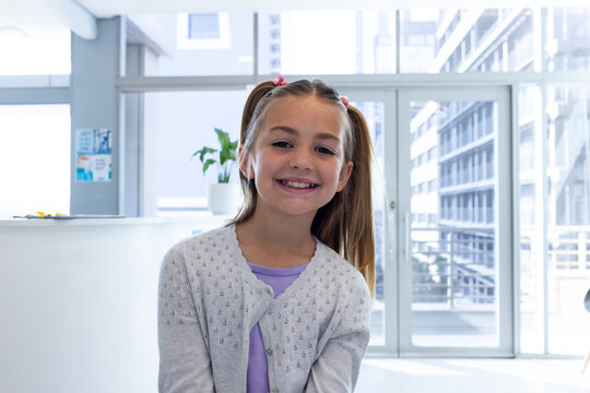 Happy caucasian girl patient with long hair in pigtails smiling in hospital waiting room, copy space
