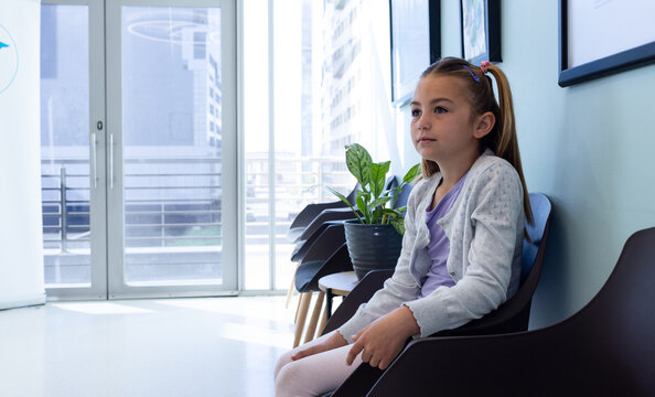Happy caucasian girl patient with long hair in pigtails sitting in hospital waiting room, copy space