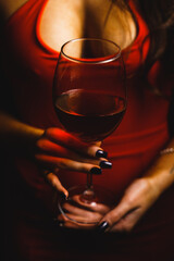 A glass of red wine in the hands of a sexy woman in a red dress