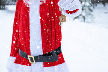 House key with keychain cottage in hands of Santa Claus outdoor in snow. Deal for real estate,...