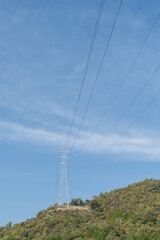 秋晴れの青空をバックに立つ里山に設置された高圧線の鉄塔