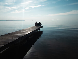 Couple of girls contemplate the sunset sitting on the dock