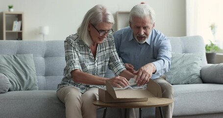 Happy surprised older mature couple cardboard box at home, taking picture book, watching pages in received family photo album with joy, smiling, excitements - Powered by Adobe