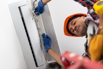 A man unscrews an air conditioner on the wall with a screwdriver. repair and maintenance of the split system.