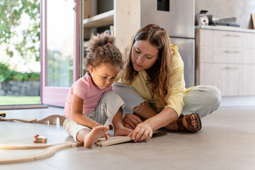 Mother and Child Playing with Toy Train - A mother and her biracial daughter assemble a wooden train set, a heartwarming scene of family bonding and playful learning.