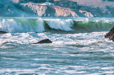 Wave splashes close-up. Crystal clear sea water hitting rock formations in the ocean in San Francisco Bay, blue water, pastel colors.