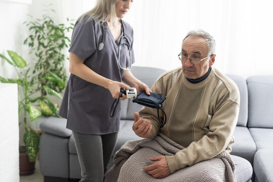 Smiling young nurse taking old man's blood pressure