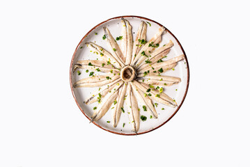 Pickled anchovies with garlic and parsley on a round rustic plate and white background, top view.