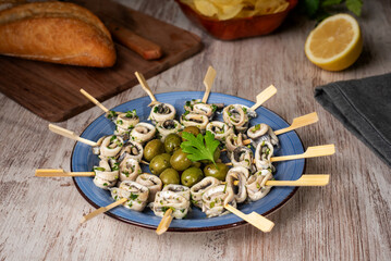 Dish with pickled anchovies pierced on toothpicks and seasoned with garlic and parsley and some olives to accompany, ready to eat.