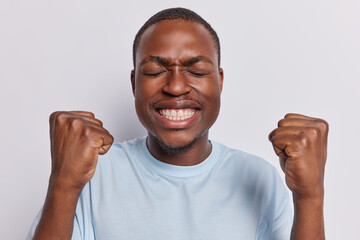 Happy thrilled dark skinned man with small beard clenching fists celebrating success enjoying...