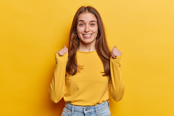 Positive European woman hopes for good luck clenches fists has big expectations for something nice happen dressed in casual clothing isolated over vivid yellow background. People wish desire concept