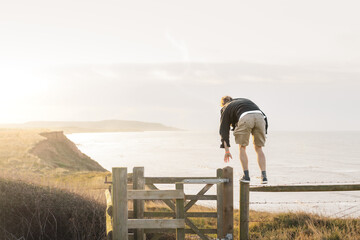 A man climbing a fence on a clifftop with a sunning sea view