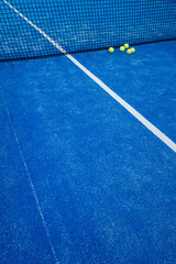 blue paddle tennis court net with five balls nearby, racket sports concept
