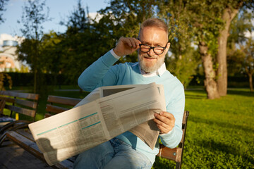 Fototapeta premium Confident bearded mature man reading daily newspaper on park bench