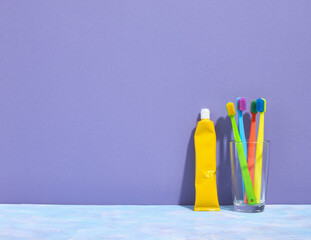 Several colored toothbrushes stand in a glass. A yellow tube of refreshing toothpaste for dental...