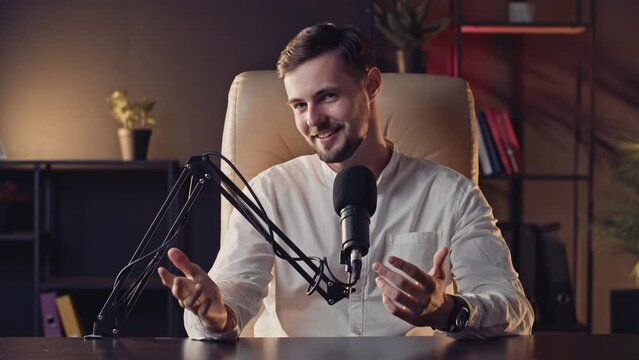 Positive caucasian podcaster wavings hand during saying hello to subscribers. Blogger recording podcast program in social networks. Famous influencer talking microphone at professional studio