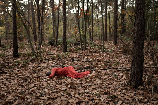 woman in red dress laying down alone in forest in autumn