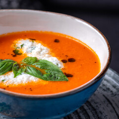 Bowl of tomato soup drizzled with cream and garnish with leaves of fresh green basil