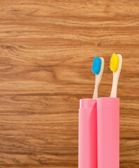 Classic bamboo toothbrushes in a pink container on a wooden background. Cleaning the teeth. Copy space for text.