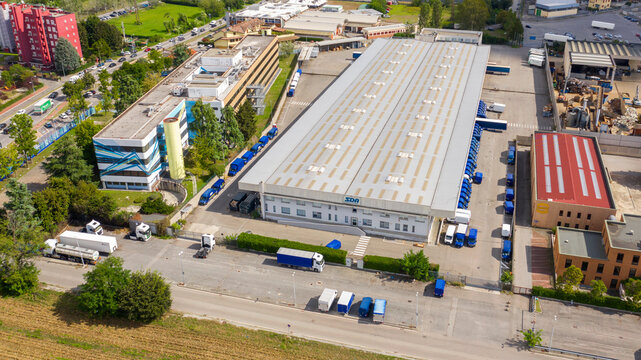 Vimodrone, Italy - November, 2023: Aerial view of a large shed of the Sda shipping company. Warehouse for loading and unloading parcels. Many trucks are parked around the facility. Industrial area.