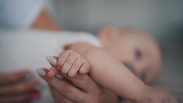 Baby touches mommy's hand grasping reflex of infants, affection formation, hands close-up view. Newborn child holding hand of mother. Childhood motherhood, babycare and kid's protection concept.