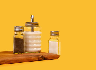 Glass jars with sugar, salt and pepper on a kitchen wooden board. Copy space for text.
