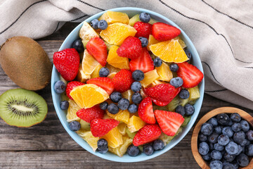 Delicious fresh fruit salad and ingredients in bowl on wooden table, flat lay