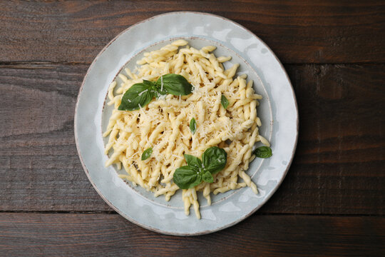 Plate of delicious trofie pasta with cheese and basil leaves on wooden table, top view