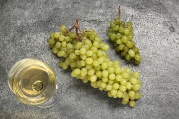 Delicious fresh green grapes and glass of wine on grey textured table, flat lay